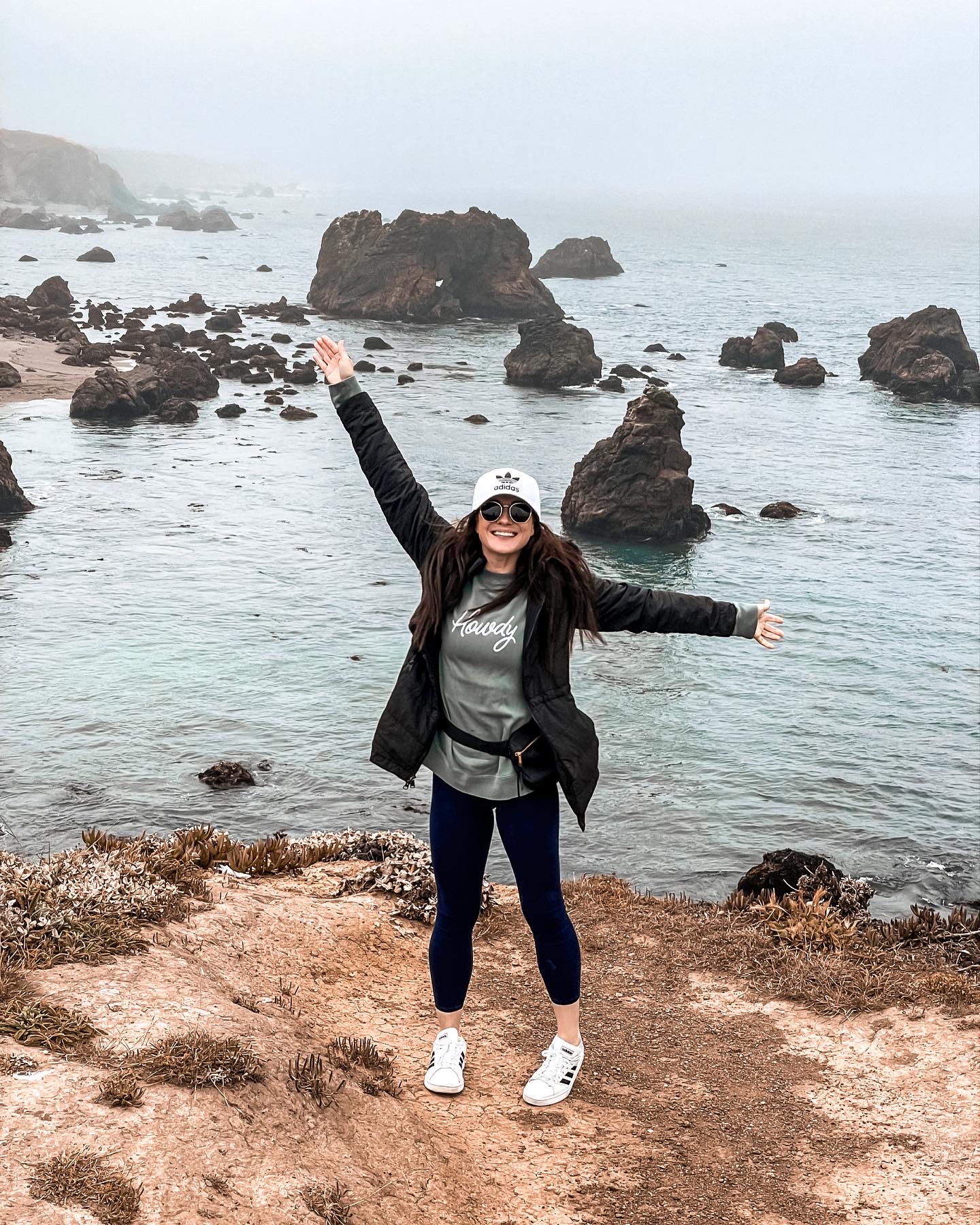 Me smiling and raising my arms in excitement while standing on a rocky coastline in California during a trip to the Redwood Forest in May 2022. This was right before I found out I was living with cPTSD.