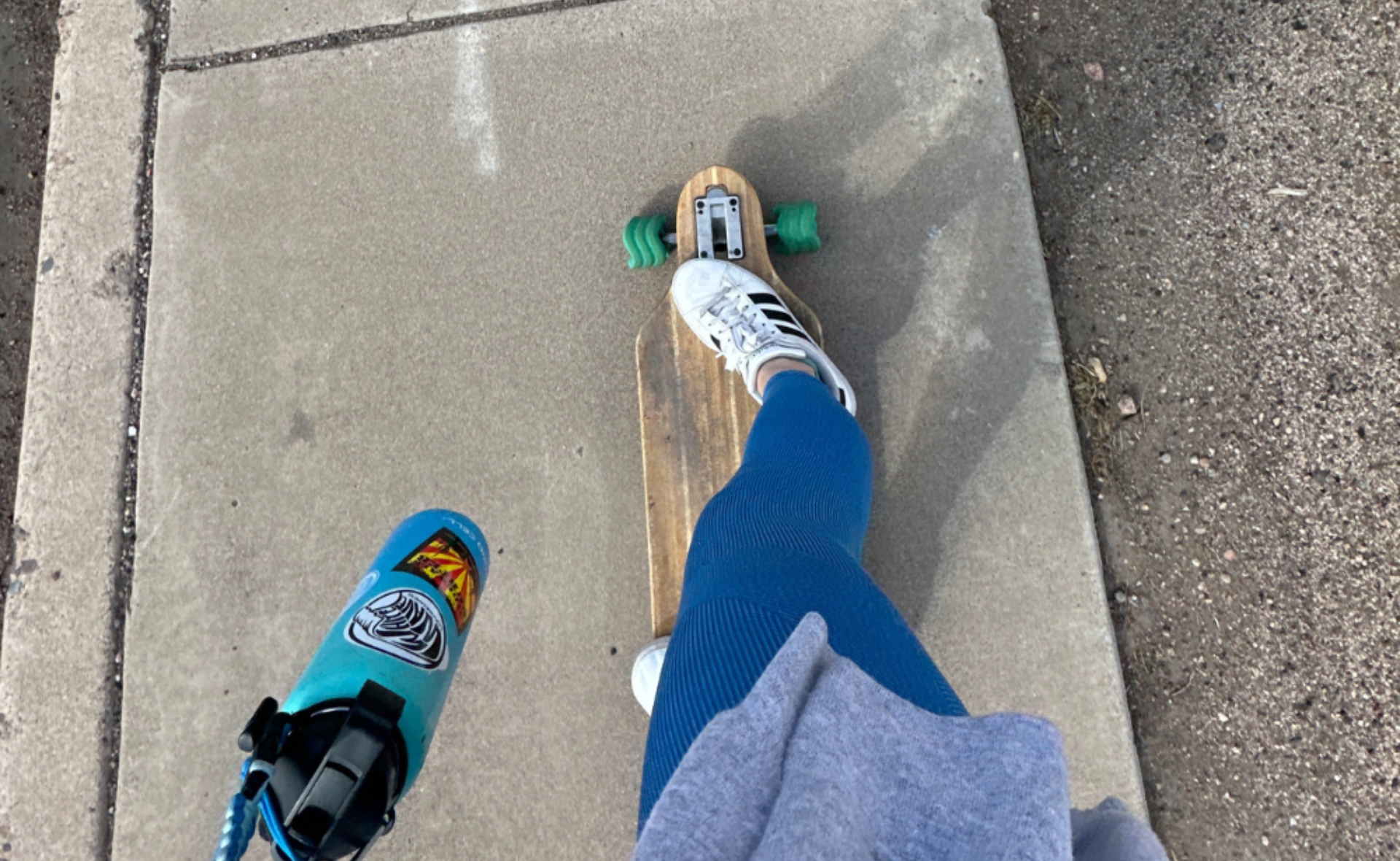 Me standing on a skateboard, wearing blue leggings and white sneakers, holding a blue water bottle decorated with stickers, on a concrete sidewalk. Fall Forward - A Personal Story Towards Resilience