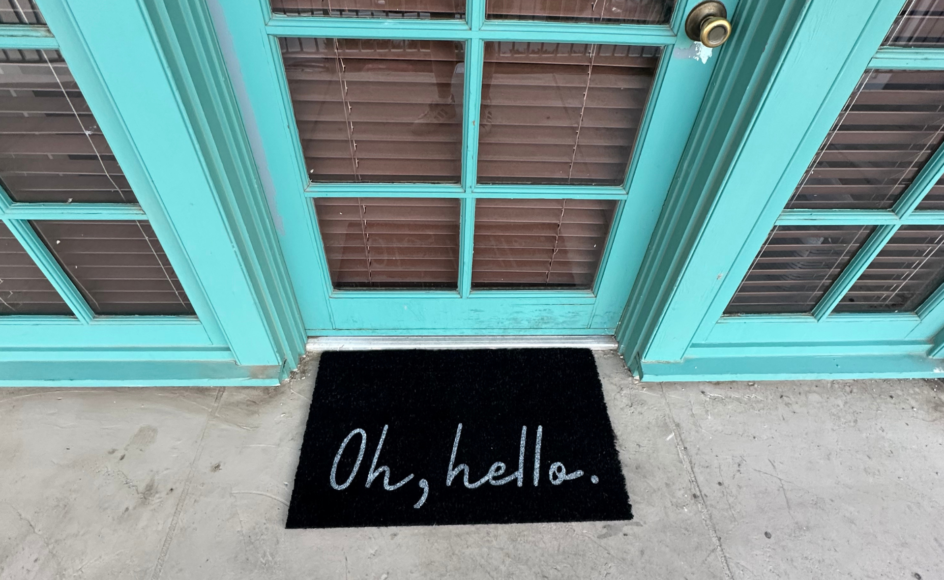 Moving into my own apartment. Cute target doormat that says "Oh, hello" on it in front of a teal door with windows.